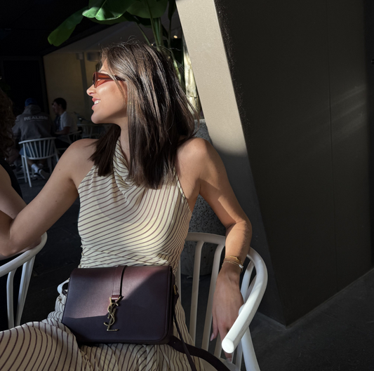 A burgundy Saint Laurent satchel crossbody bag with a gold-finish logo, displayed against a white background.
