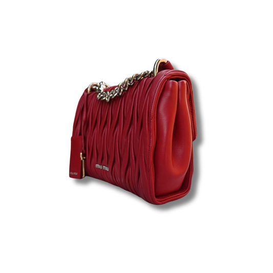 A red Miu Miu matelassé nappa leather shoulder bag with a textured finish, featuring a logo on the front and a chain strap.