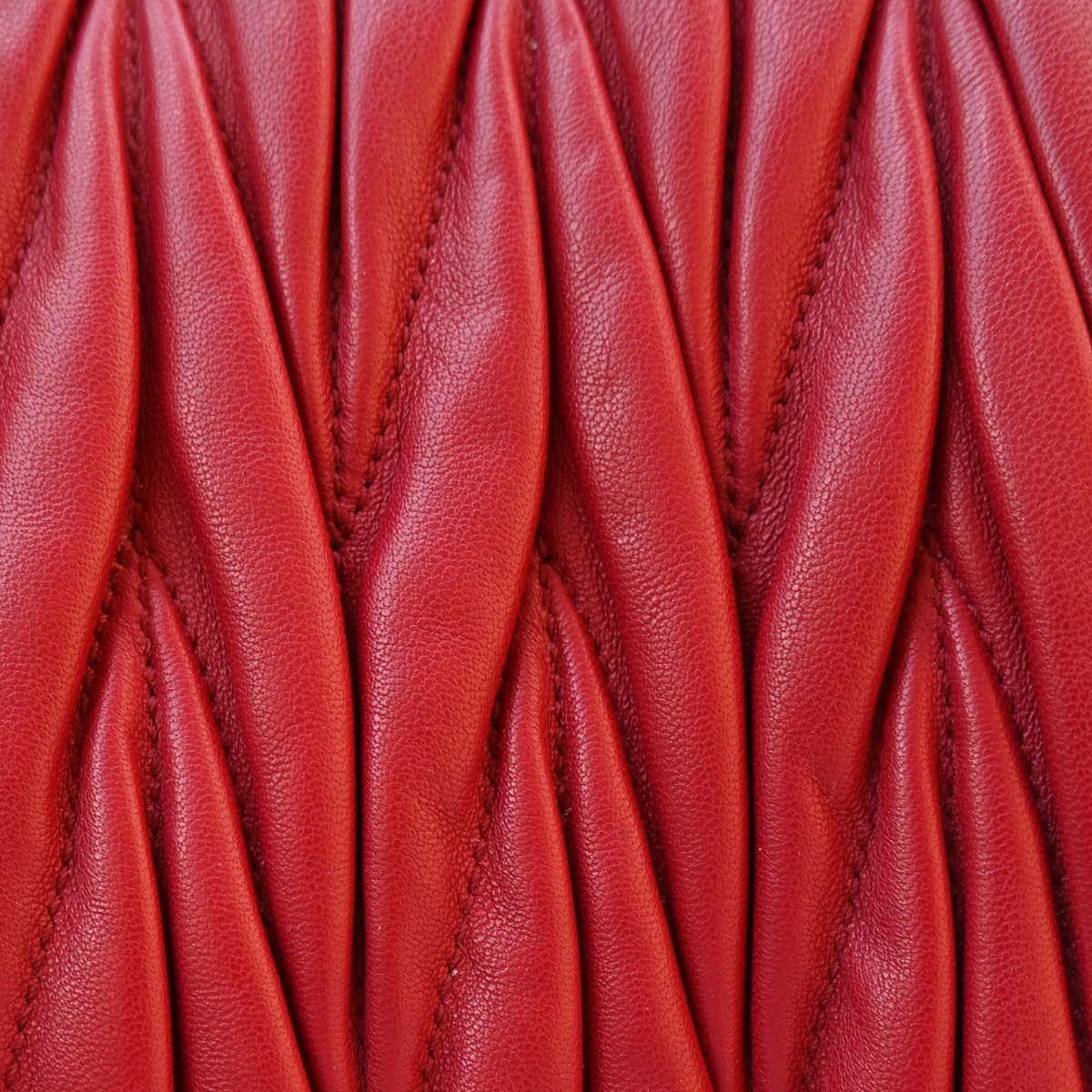 A red Miu Miu matelassé nappa leather shoulder bag with a textured finish, featuring a logo on the front and a chain strap.