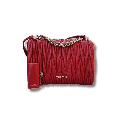 A red Miu Miu matelassé nappa leather shoulder bag with a textured finish, featuring a logo on the front and a chain strap.
