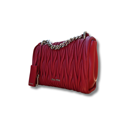 A red Miu Miu matelassé nappa leather shoulder bag with a textured finish, featuring a logo on the front and a chain strap.