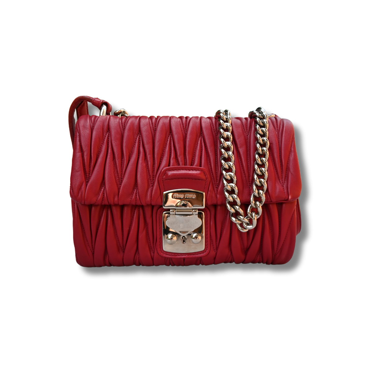 A red Miu Miu matelassé nappa leather shoulder bag with a textured finish, featuring a logo on the front and a chain strap.