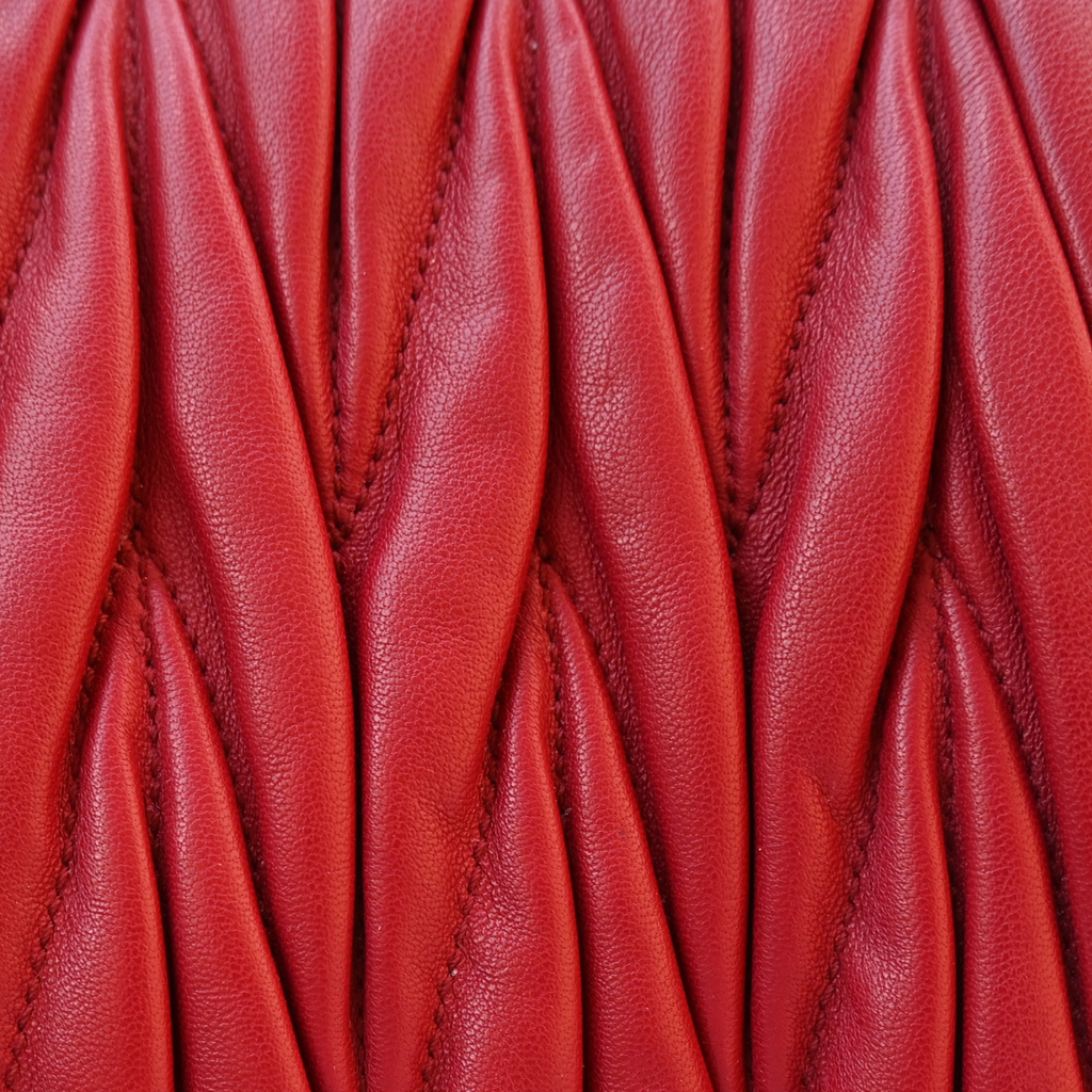 A red Miu Miu matelassé nappa leather shoulder bag with a textured finish, featuring a logo on the front and a chain strap.