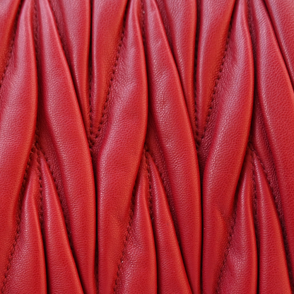 A red Miu Miu matelassé nappa leather shoulder bag with a textured finish, featuring a logo on the front and a chain strap.